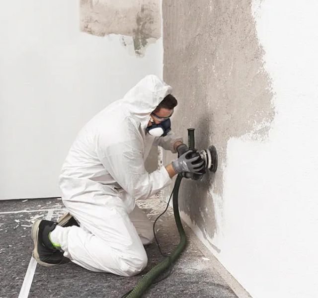 A man dressed in a white suit and protective gear is painting a wall, indicating a mold removal service in Chicago, IL.